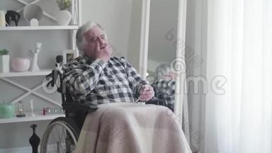 成熟的白种人白发老人坐在轮椅上，头痛得厉害。 老年